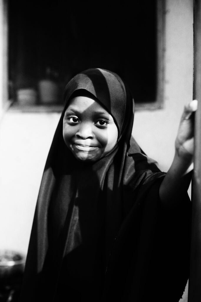 Black and white portrait of a young girl in hijab smiling confidently indoors.